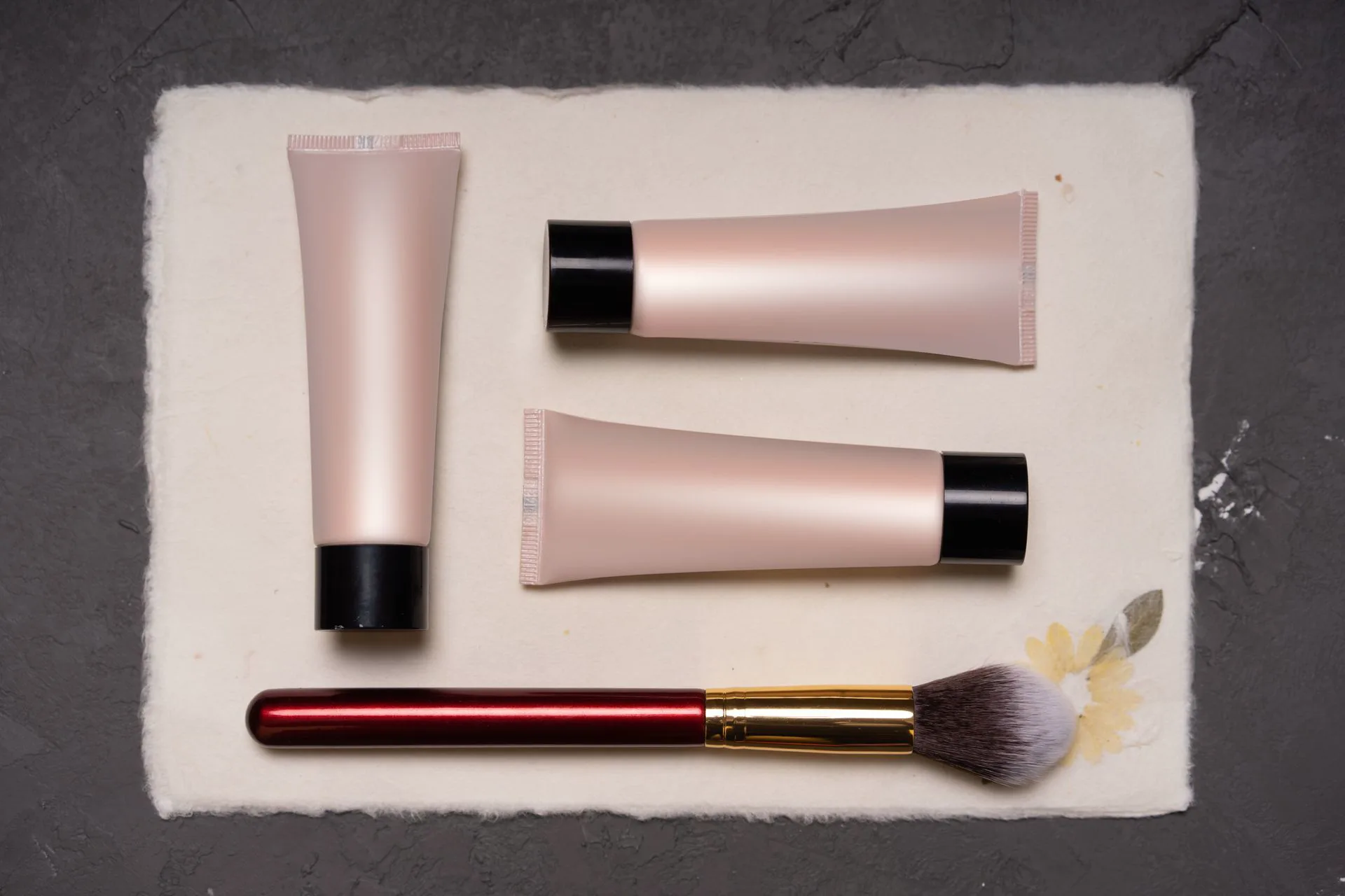 Tubes de soin et pinceau posés sur un papier crème